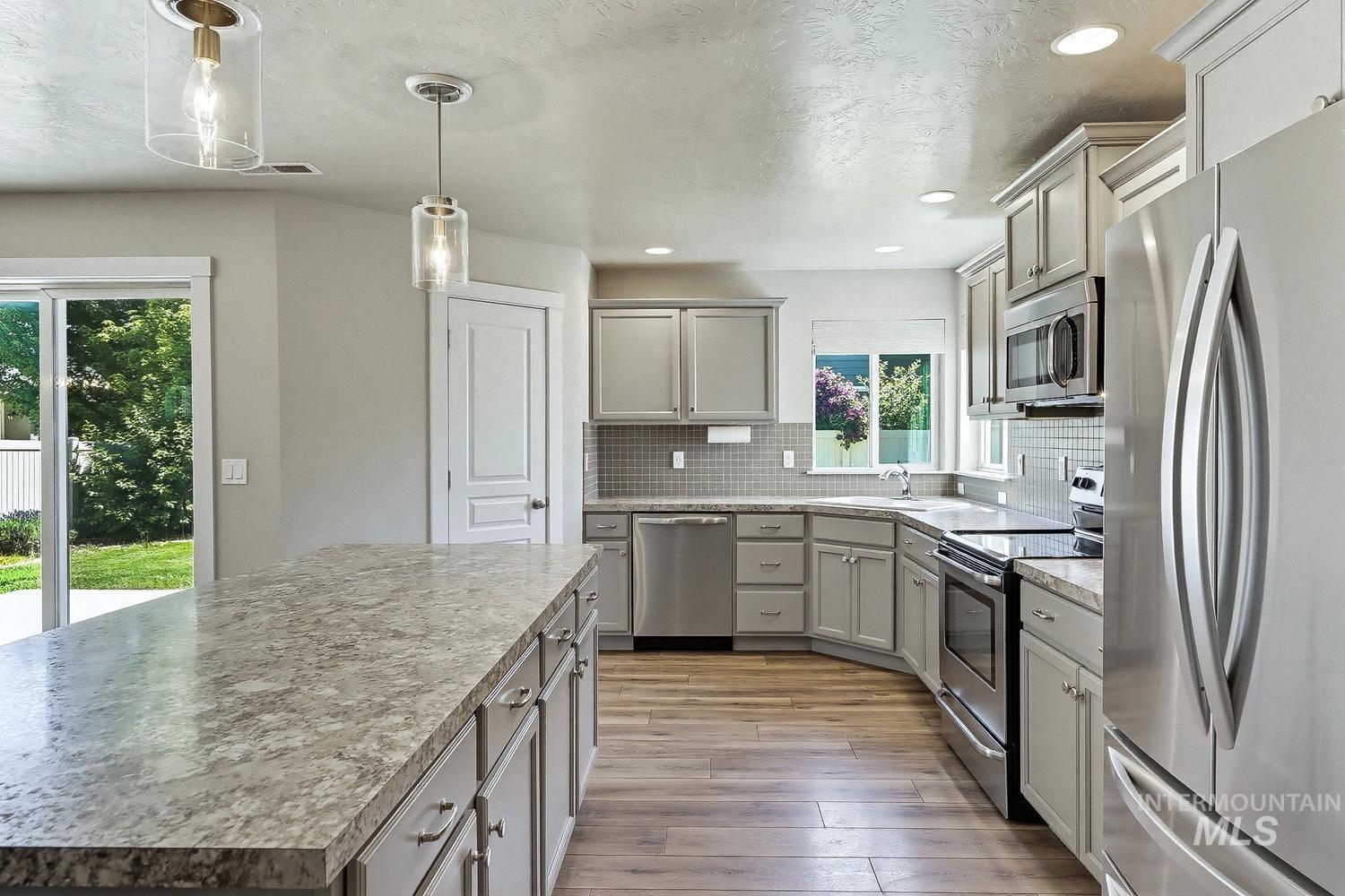 846 North Hidden View Way Star, ID 83669 - Photo 12 of 49 Kitchen featuring an expansive island with a light-toned countertop, stainless steel appliances, wood-finish flooring, a mosaic tile backsplash, and recessed lighting