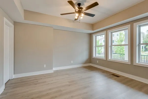 an empty room with wooden floor fan and windows