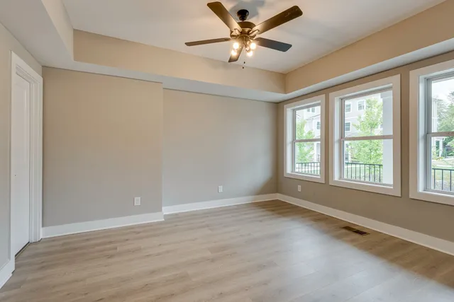 an empty room with wooden floor fan and windows
