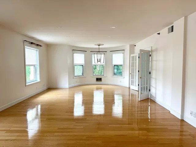 a view of an empty room with window and wooden floor