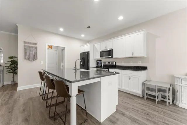 a kitchen with stainless steel appliances kitchen island granite countertop a refrigerator a stove a sink a dining table and chairs with wooden floor