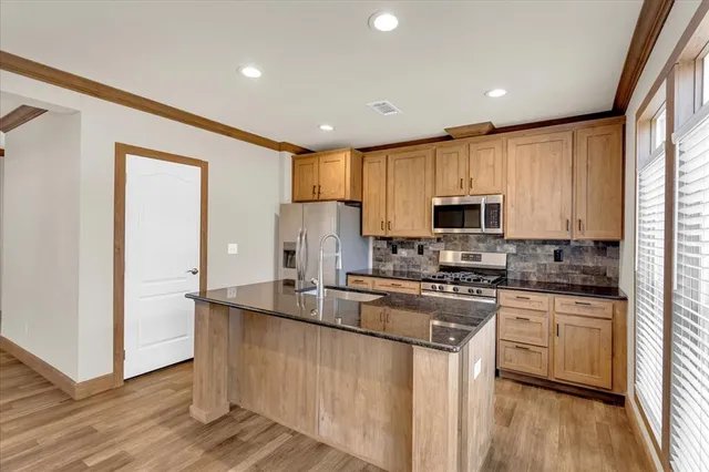 a kitchen with stainless steel appliances granite countertop a stove a sink a refrigerator and white cabinets with wooden floor