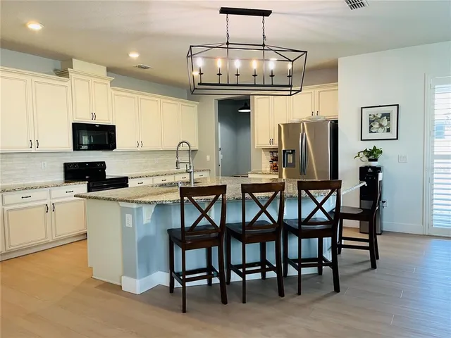 a kitchen with stainless steel appliances granite countertop a dining table chairs refrigerator and microwave