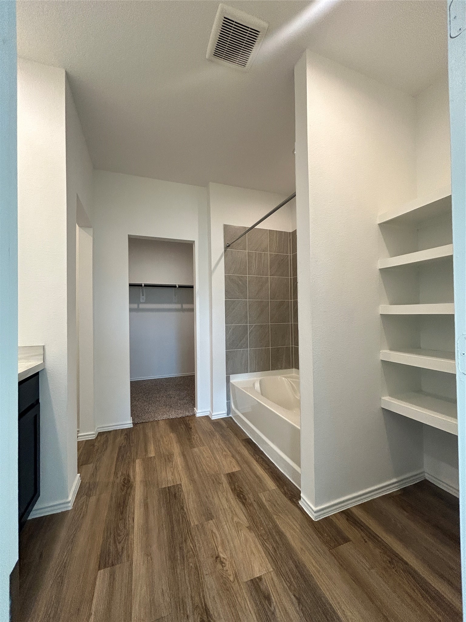 1739 Royal Rim Drive Houston, TX 77014 - Photo 15 of 20 The modern bathroom has wood-style flooring, a bathtub with a tiled surround, open shelving, and a walk-in closet. The space is bright and spacious, providing a clean and functional layout.