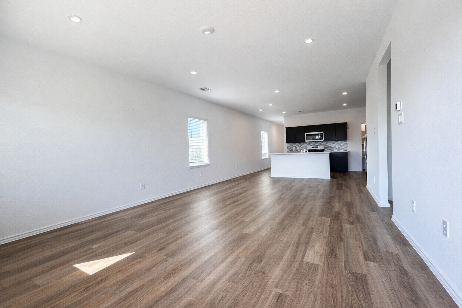 1739 Royal Rim Drive Houston, TX 77014 - Photo 7 of 20 Spacious, open-concept living area with modern hardwood flooring and recessed lighting. The room leads into a sleek kitchen equipped with stainless steel appliances and a stylish backsplash. The space is bright and airy, perfect for entertaining.