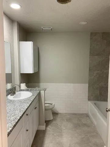 a bathroom with a granite countertop sink a toilet and bathtub