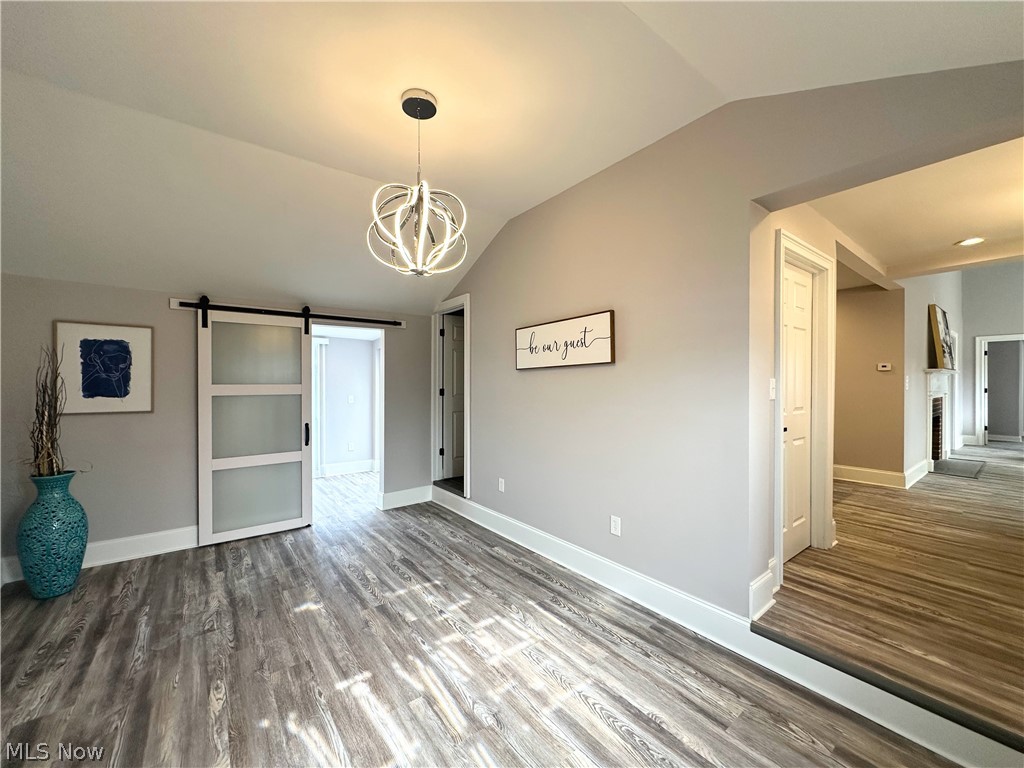 Unfurnished dining area with a barn door, a chandelier, wood finished floors, and a brick fireplace