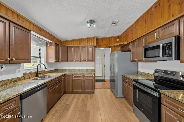 a kitchen with stainless steel appliances granite countertop a sink a stove top oven a refrigerator with wooden floors and granite counter tops