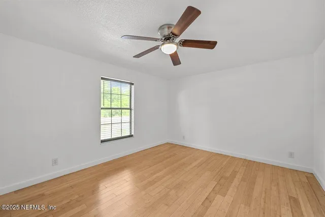 a view of empty room with wooden floor and fan