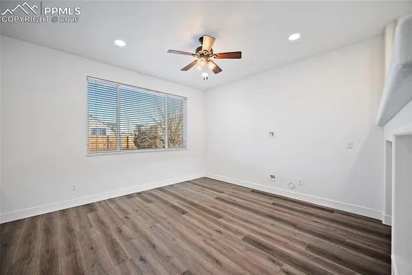 an empty room with wooden floor ceiling fan and windows