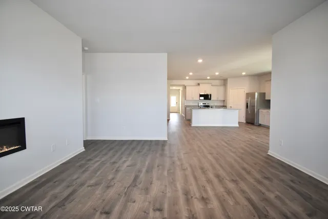 a large kitchen with stainless steel appliances granite countertop a stove a sink a refrigerator and white cabinets with wooden floor