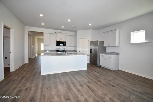 a large kitchen with stainless steel appliances granite countertop a stove a sink a refrigerator and white cabinets with wooden floor