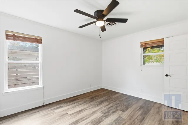 an empty room with wooden floor ceiling fan and windows