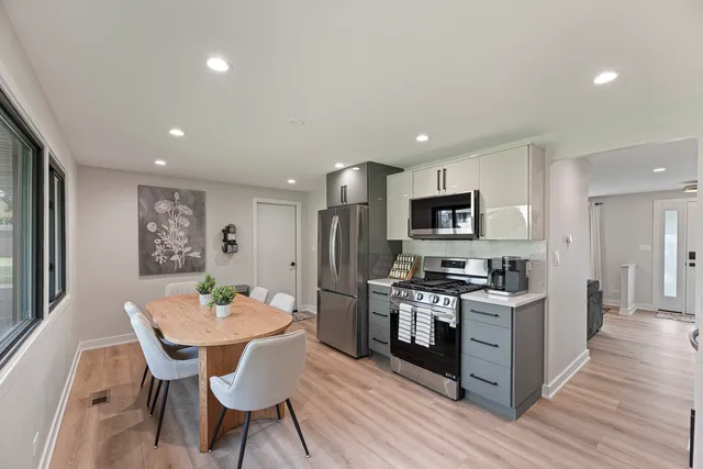 a kitchen with stainless steel appliances kitchen island granite countertop a stove top oven a sink dishwasher a dining table and chairs with wooden floor