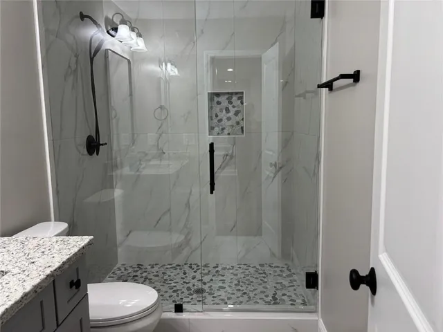 a bathroom with a granite countertop shower a toilet and a sink
