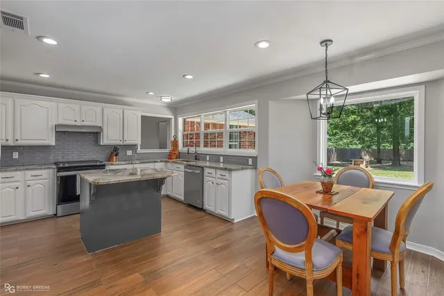 a kitchen with stainless steel appliances granite countertop a stove top oven a sink dishwasher a dining table and chairs with wooden floor