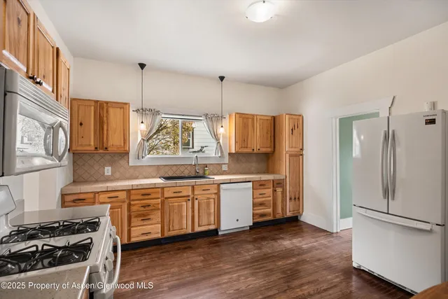 a kitchen with stainless steel appliances granite countertop a refrigerator a sink dishwasher a stove and white countertops with wooden floor