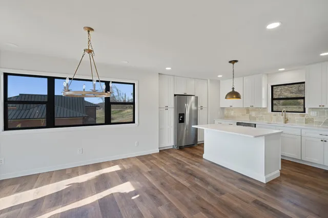 a kitchen with stainless steel appliances granite countertop a refrigerator a sink dishwasher a oven and white cabinets with wooden floor