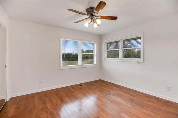a view of an empty room with wooden floor and a chandelier fan