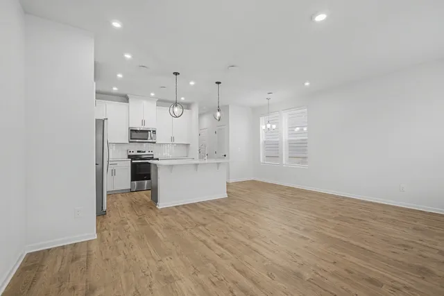 a large white kitchen with kitchen island a stove a sink dishwasher and white cabinets with wooden floor