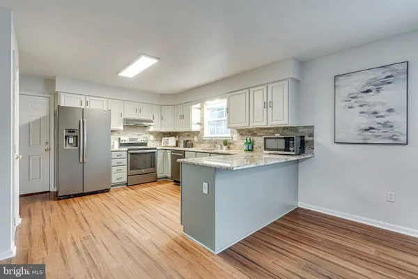 a kitchen with stainless steel appliances granite countertop a refrigerator a stove and white cabinets with wooden floor