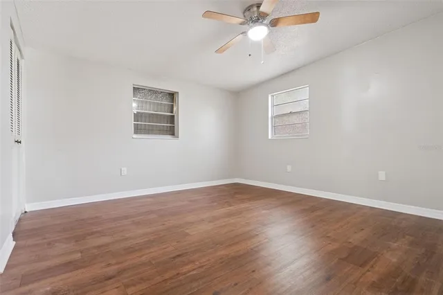 an empty room with wooden floor fan and windows