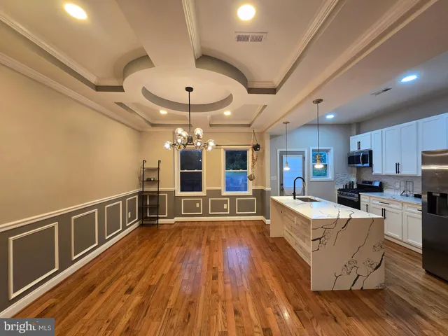 a view of an empty room with wooden floor and a kitchen