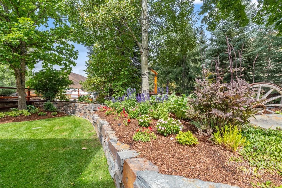 106 Hidden Hollow Road Hailey, ID 83333 - Photo 3 of 49 Expansive yard featuring a manicured lawn, stone retaining wall, diverse landscaping with various plantings, and mature trees