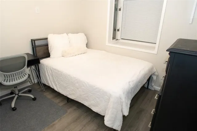 a bedroom with a bed a chair and a potted plant on the dresser