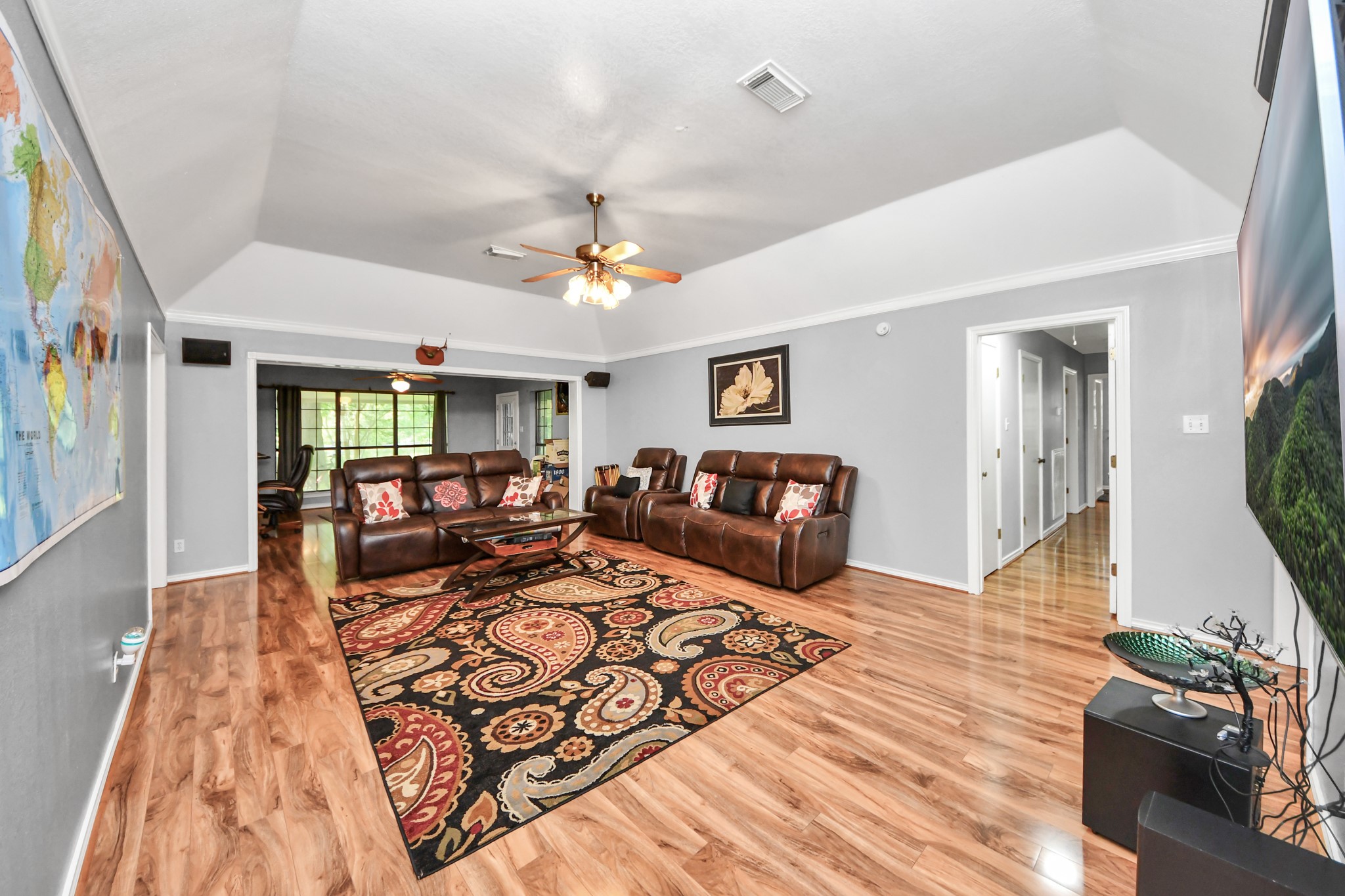 12746 Roy Road Pearland, TX 77581 - Photo 26 of 47 This spacious living room features polished wood flooring, a ceiling fan, and ample natural light from large windows. It includes a cozy seating area with leather couches and a colorful area rug. The room has a modern, open feel with neutral walls and direct access to a hallway and adjacent dining area.