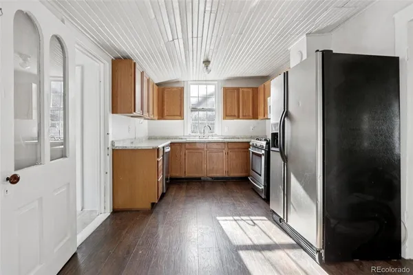 a kitchen with stainless steel appliances granite countertop a refrigerator a sink dishwasher a stove and white countertops with wooden floor