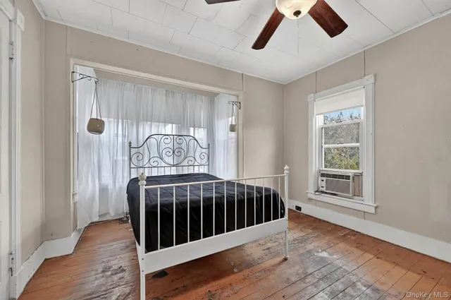 a view of a bedroom with wooden floor windows a ceiling fan and windows