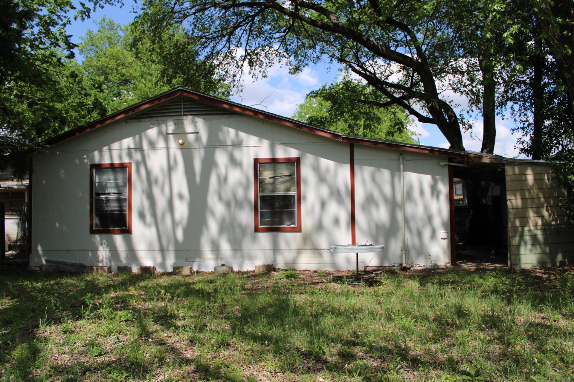 3017 Lyons Road Austin, TX 78702 - Photo 6 of 16 The property features a white exterior with brown trim around the windows and a natural setting with mature trees and a grassy area