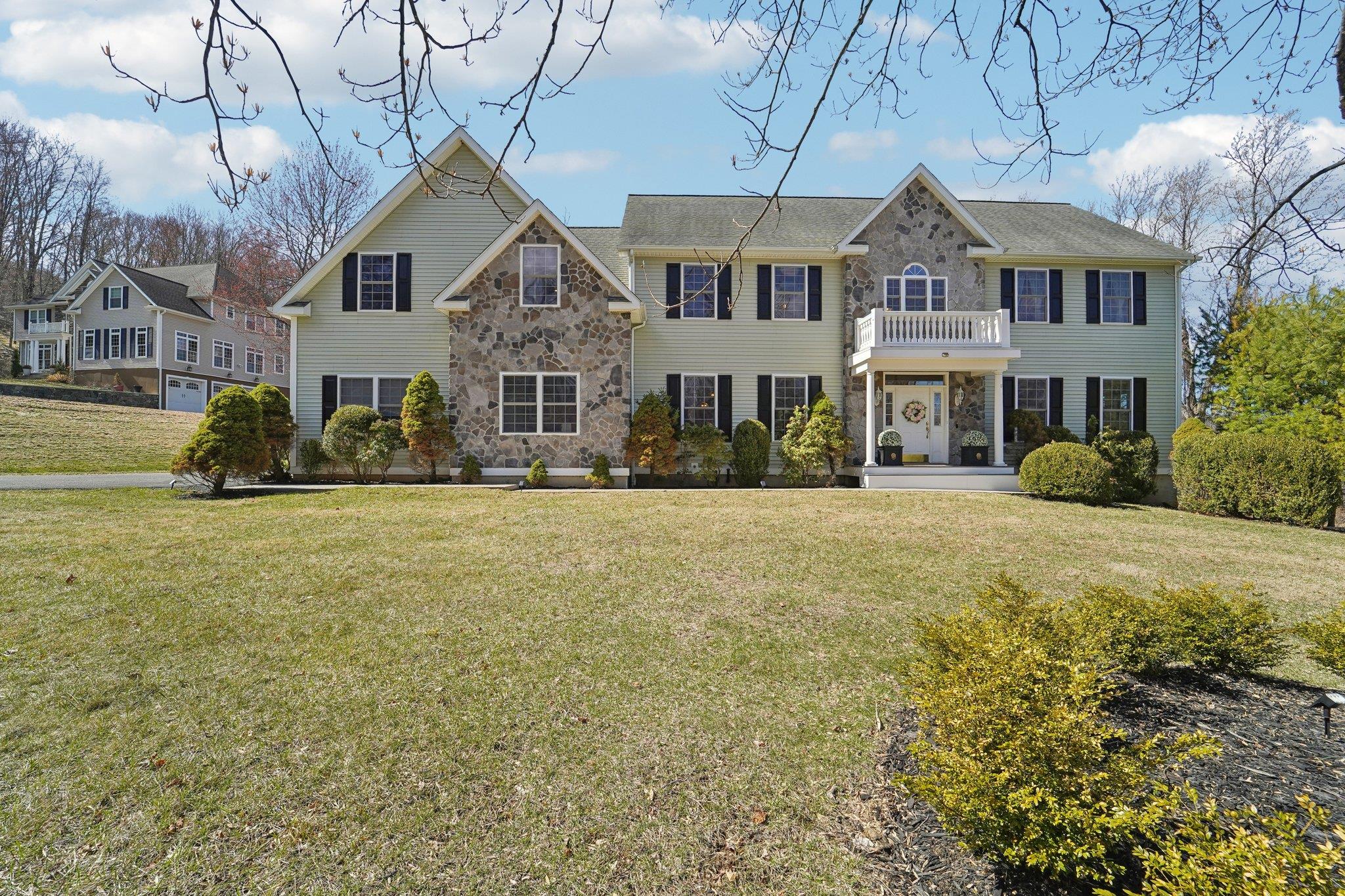 View of front of property with stone siding, a front lawn, and a balcony