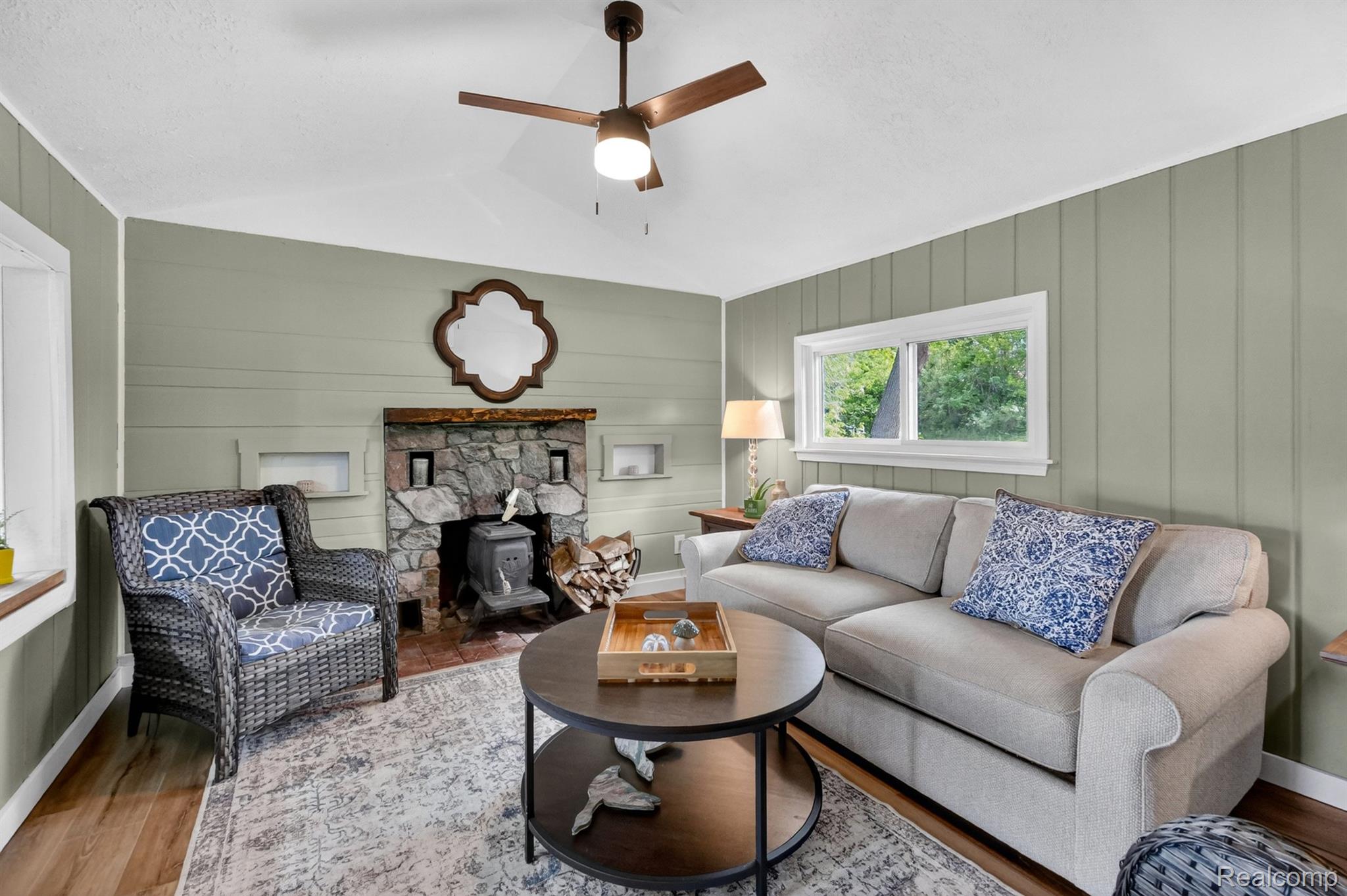 1717 Triangle Lake Road Howell, MI 48843 - Photo 39 of 58 Living area featuring a stone-clad fireplace with a wood-burning stove insert, wood-finish flooring, and vertical paneling on the walls