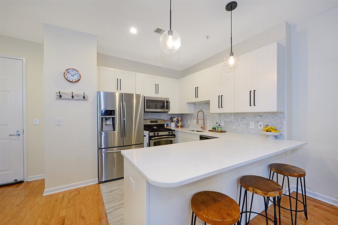 a kitchen with stainless steel appliances a refrigerator a sink a stove white cabinets and chairs
