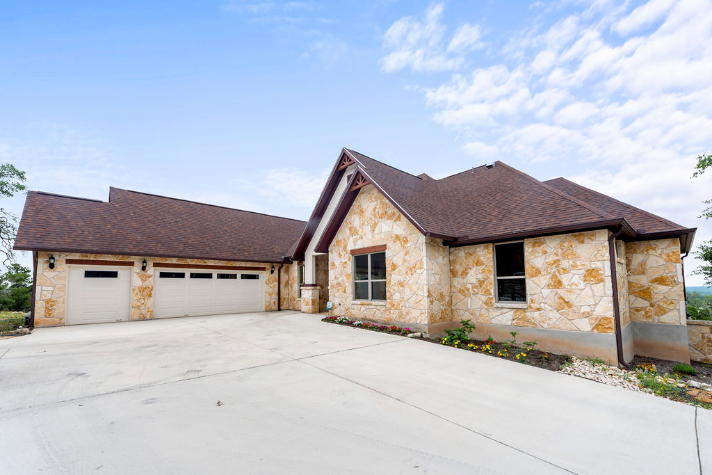 213 Lets Roll Drive Fischer, TX 78623 - Photo 34 of 38 View of front of home featuring stone siding, a garage, roof with shingles, and concrete driveway