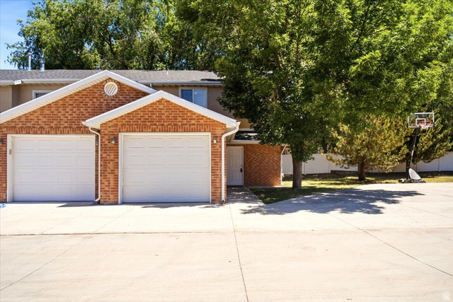 449 West 200 North, Unit 3 Bountiful, UT 84010 - Photo 2 of 23 Brick exterior featuring two white garage doors, a concrete driveway, and mature landscaping