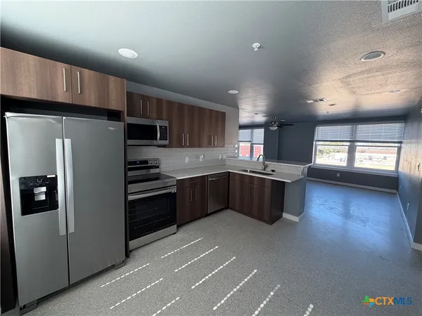 a kitchen with stainless steel appliances kitchen island granite countertop a refrigerator a sink dishwasher a stove and a microwave oven with wooden floor