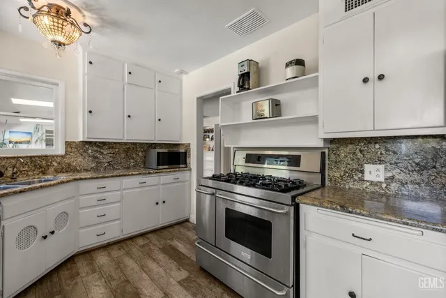 a kitchen with granite countertop a stove a sink dishwasher and white cabinets with wooden floor