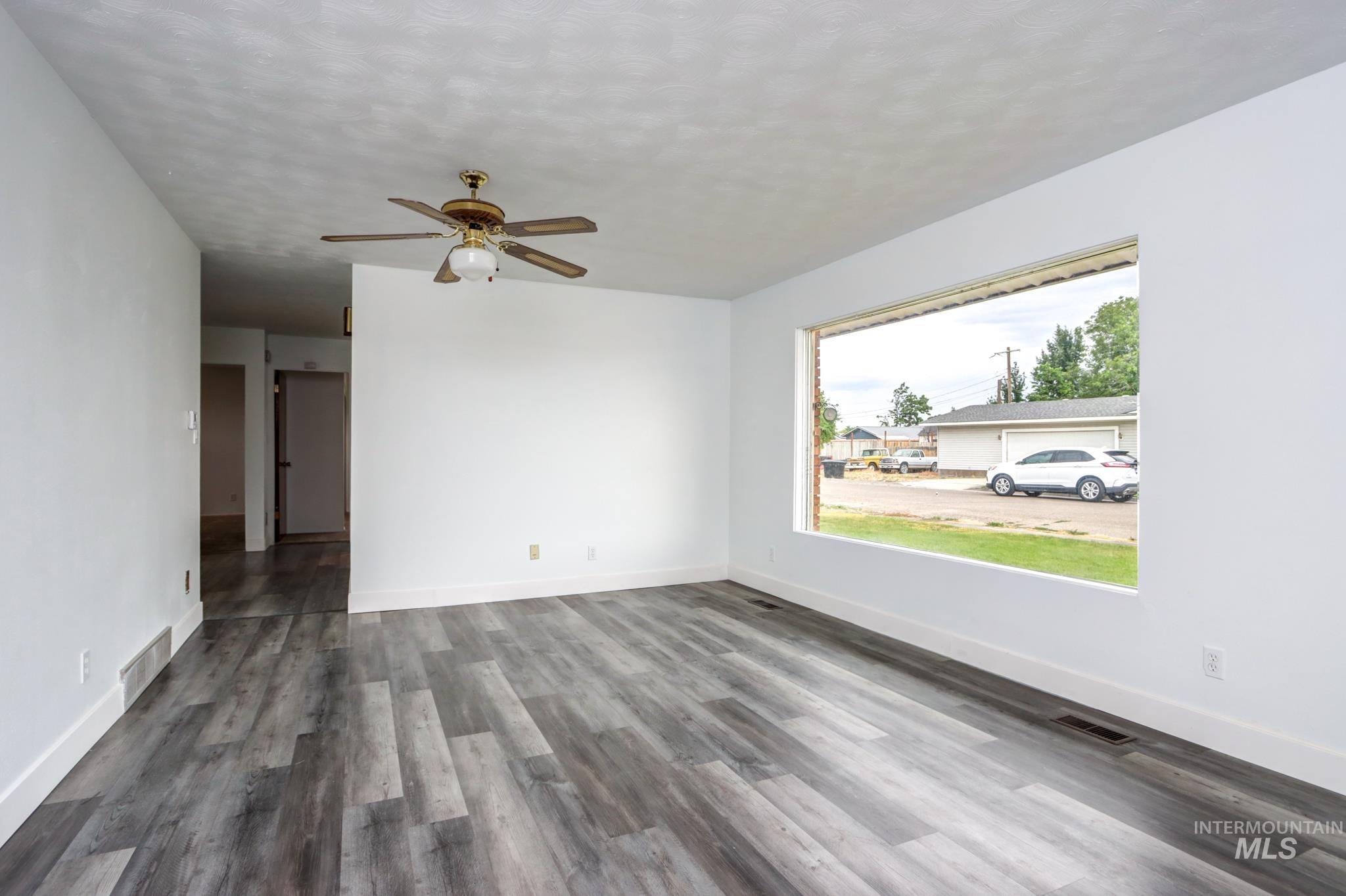 801 Thompson Avenue Nyssa, OR 97913 - Photo 2 of 46 Spacious interior featuring wide-plank wood-finish flooring, a large picture window, a ceiling fan with integrated lighting, white walls, and white baseboards