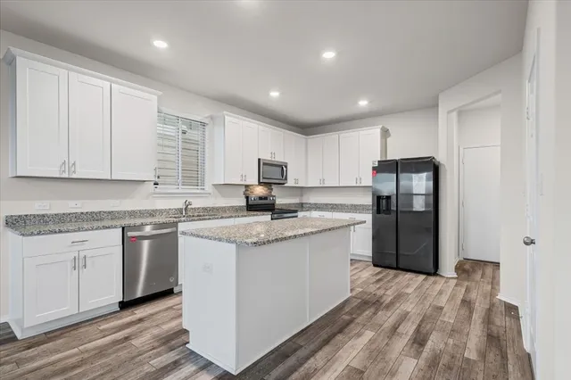 a kitchen with stainless steel appliances granite countertop a refrigerator a sink dishwasher a stove and white countertops with wooden floor