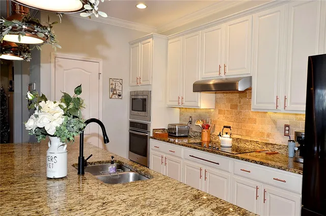 a kitchen with stainless steel appliances kitchen island granite countertop a refrigerator a sink dishwasher and white cabinets with wooden floor