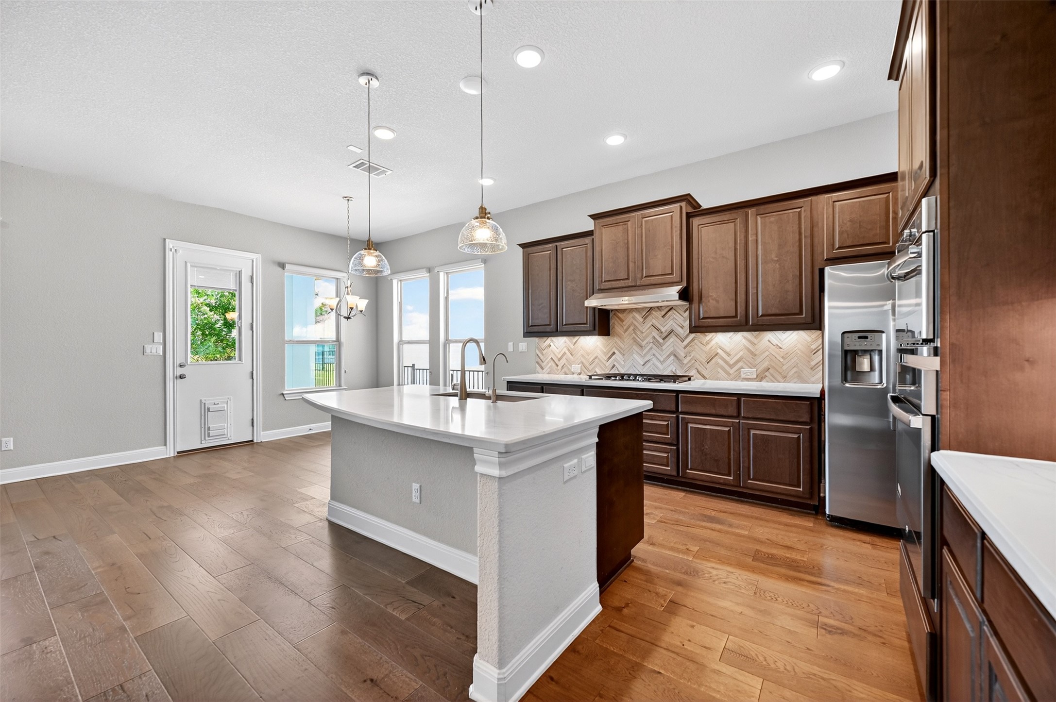 1201 Positano Pass Leander, TX 78641 - Photo 10 of 40 Modern kitchen featuring a central island with a white countertop and undermount sink, rich wood cabinetry, stainless steel appliances, and a herringbone pattern tile backsplash