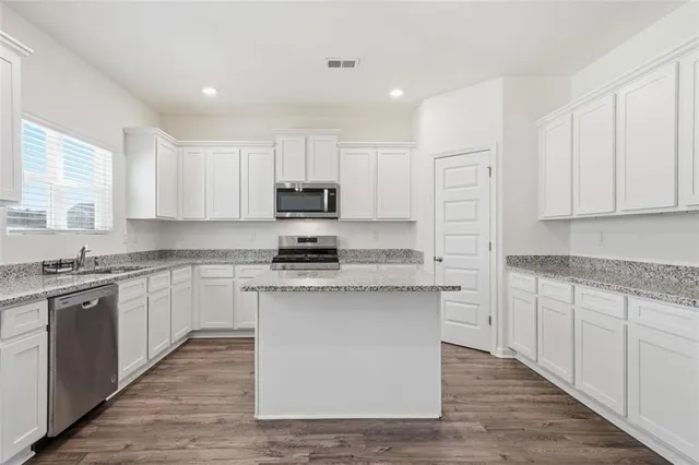 a kitchen with stainless steel appliances granite countertop a stove top oven a sink dishwasher and a refrigerator with wooden floor