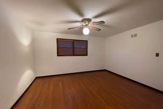 an empty room with wooden floor chandelier fan and windows