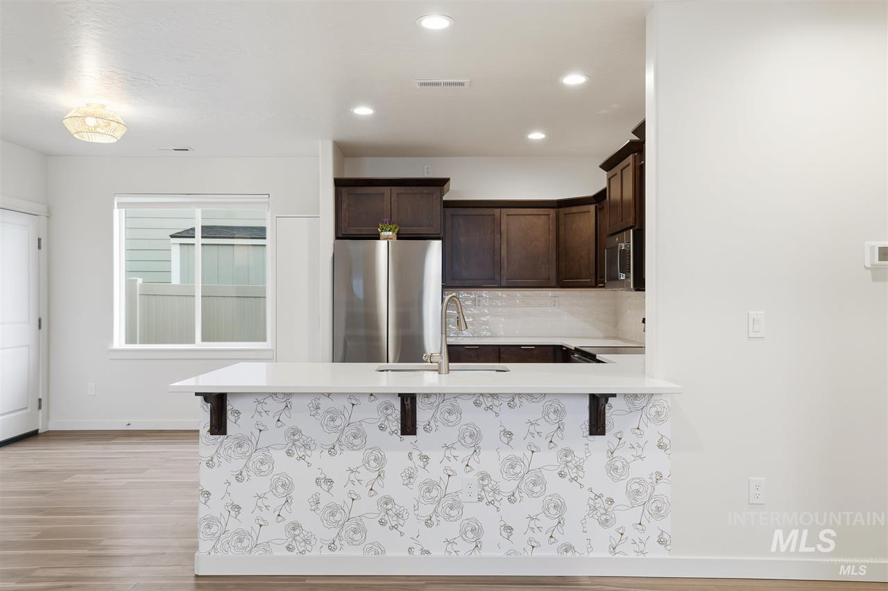 449 West Winnipeg Street Meridian, ID 83642 - Photo 10 of 49 Kitchen with dark brown cabinetry, a kitchen breakfast bar, stainless steel appliances, light wood-style flooring, and backsplash