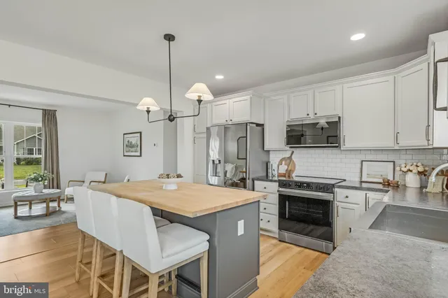 a open kitchen with stainless steel appliances granite countertop a stove top oven a sink dishwasher a dining table and chairs with wooden floor