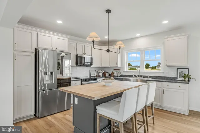 a kitchen with stainless steel appliances granite countertop a refrigerator a sink dishwasher a stove and white cabinets with wooden floor