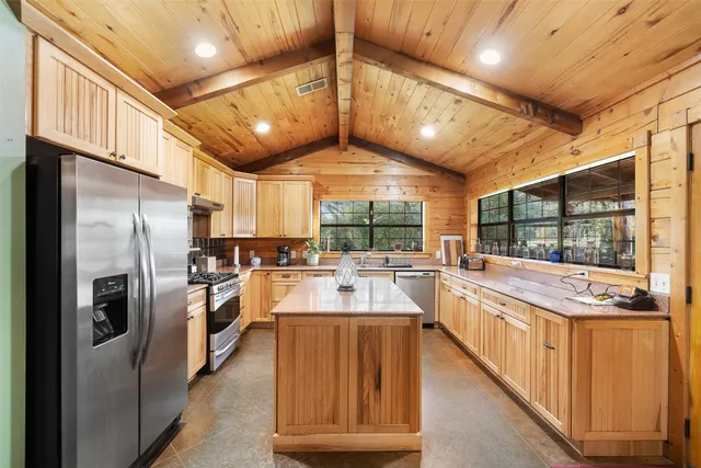 a large kitchen with kitchen island a large window a sink and stainless steel appliances
